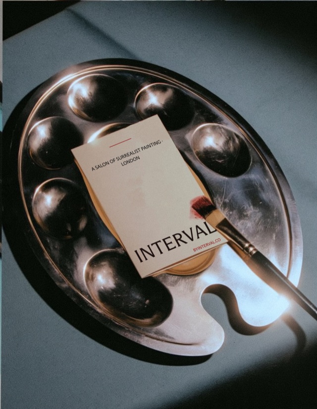 The Interval card resting on a silver painter's palette with a brush