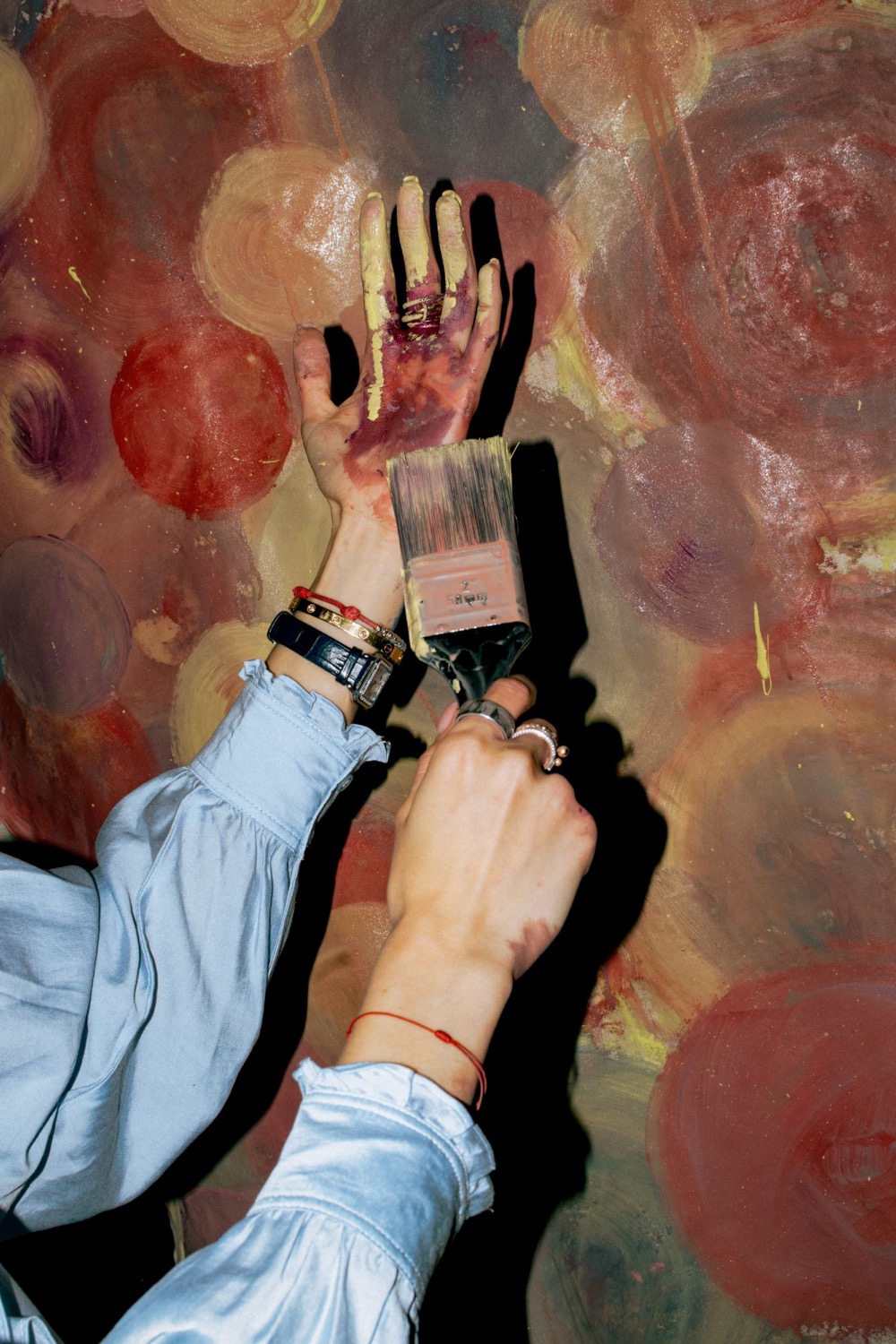 Two hands, one covered in paint, working a wide brush across the floor cloth at a painting evening for women in east London