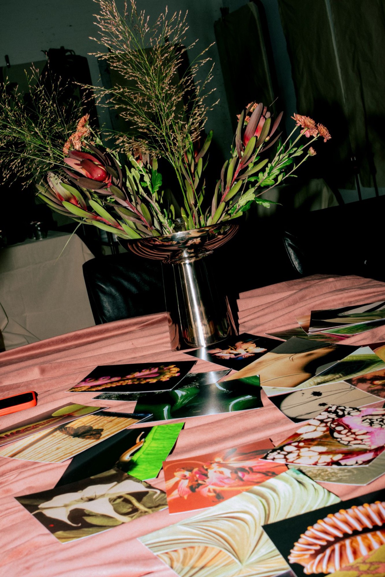 The reference table before an evening begins: printed images spread across a pink cloth beside a vase of flowers, at a surrealist painting salon in London