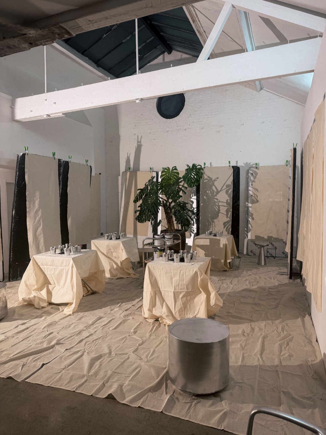 The room set before anyone arrives: lengths of calico hung and clipped, cloth-covered tables of glasses, at a painting evening in London